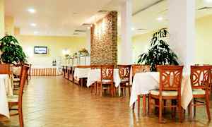 Kuva ruokasalista, jossa pöytiä ja puutuoleja, valkoiset pöytäliinat, kasveja ja buffettialue. (Tekoälyn luoma teksti)