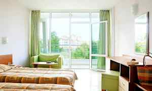 Hotellihuone, jossa on parivuoteet, kirjoituspöytä ja avoin ikkuna parvekkeelle näkymällä. (Tekoälyn luoma teksti)