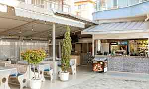 Ulkoterassi, jossa pöydät ja tuolit, ympärillä kasveja ja baaritiski. (Tekoälyn luoma teksti)