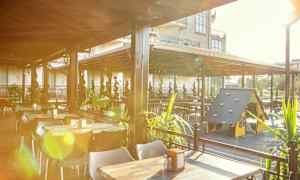 Ulkoterassi, jossa on pöytiä, tuoleja ja lasten leikkipaikka katoksen alla. (Tekoälyn luoma teksti)