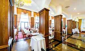 Tyylikäs ravintola, jossa katetut pöydät, tummat puulattiat ja suuret ikkunat verhoilla. (Tekoälyn luoma teksti)