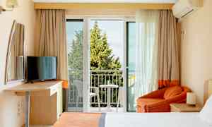 Hotellihuone, jossa parveke, sänky, nojatuoli ja televisio. (Tekoälyn luoma teksti)