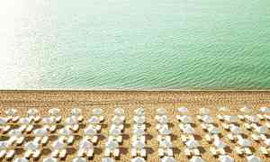 Ranta, jossa aurinkotuoleja ja varjoja rivissä lähellä turkoosia merta. (Tekoälyn luoma teksti)