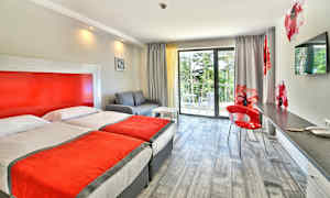 Hotellihuone, jossa on kaksi erillistä vuodetta, sohva, työpöytä ja parveke näkymällä vehreyteen. (Tekoälyn luoma teksti)