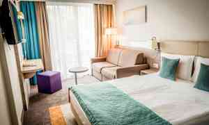 Nykyaikainen hotellihuone, jossa on parivuode, sohva ja ikkuna verhoineen. (Tekoälyn luoma teksti)