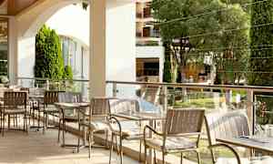 Ulkotarjoilualue, jossa on pöytiä ja tuoleja, ympäröitynä vihreillä puilla ja istutuksilla. (Tekoälyn luoma teksti)