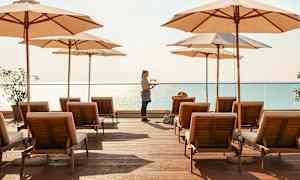 Aurinkotuoleja ja varjoja puisella terassilla meren äärellä. (Tekoälyn luoma teksti)