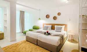 Moderni hotellihuone, jossa kaksi erillistä vuodetta, vihreä istuin ja koristeita seinällä. (Tekoälyn luoma teksti)