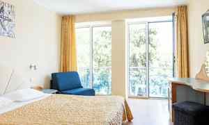 Huone, jossa sänky, sininen nojatuoli ja kirjoituspöytä, suuret ikkunat parvekkeelle. (Tekoälyn luoma teksti)