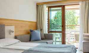 Hotellihuone, jossa on sänky, sohva ja parvekekalusteet näkyvissä lasioven läpi. (Tekoälyn luoma teksti)