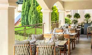 Ulkoilmaravintola katettuine pöytineen ja tuoleineen vehreässä ympäristössä. (Tekoälyn luoma teksti)