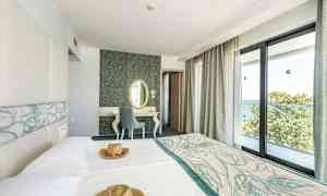 Hotellihuone, jossa on vaaleat kalusteet ja suuret ikkunat merinäköalalla. (Tekoälyn luoma teksti)