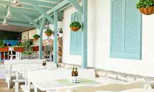 Ulkona istuma-alue, jossa valkoisiä pöytiä, riippuvia kasveja ja sinisiä puuyksityiskohtia. (Tekoälyn luoma teksti)