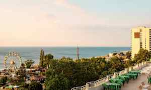 Kuvassa näkyy rannikko, meri, maailmanpyörä, vehreitä puita ja rakennuksia. (Tekoälyn luoma teksti)