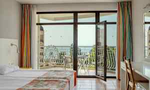 Hotellihuone, jossa parivuode, avoin parvekkeen ovi ja näkymä merelle sekä maailmanpyörälle. (Tekoälyn luoma teksti)