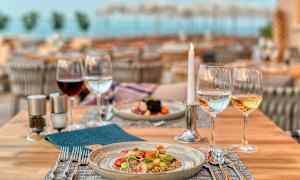 Katettu ravintolapöytä, jossa on ruokalautanen, viinilasia, vettä ja palaava kynttilä. (Tekoälyn luoma teksti)