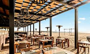 Ulkoterassi, jossa puupöytiä ja -tuoleja, hiekkarannan vieressä. (Tekoälyn luoma teksti)