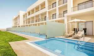 Kuva nykyaikaisesta hotellirakennuksesta, jonka edessä on yksityisiä uima-altaita ja altaiden vieressä aurinkotuoleja varjojen alla. (Tekoälyn luoma teksti)