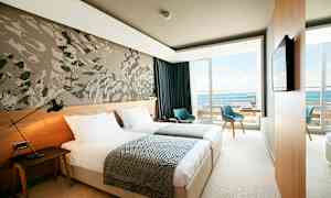 Moderni hotellihuone kahdella yhden hengen vuoteella, seinäkoristeella ja parvekkeella, jolta on näkymä merelle. (Tekoälyn luoma teksti)