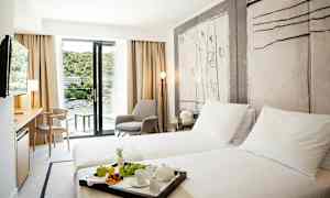 Hotellihuone, jossa on kaksi yhden hengen vuodetta, oleskelualue ja parveke, jolta avautuu näkymä vehreään ympäristöön. (Tekoälyn luoma teksti)