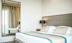 Hotellihuone, jossa on suuri sänky, tyynyt ja peili. (Tekoälyn luoma teksti)