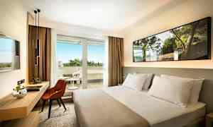 Hotellihuone, jossa sänky, työpöytä ja tuoli sekä parveke ulkokalusteilla. (Tekoälyn luoma teksti)