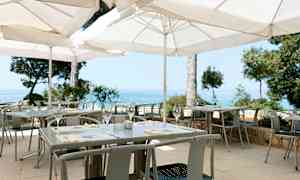 Ulkotarjoilualue, jossa valkoiset aurinkovarjot, pöydät ja tuolit sekä näkymä merelle. (Tekoälyn luoma teksti)