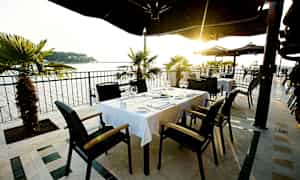 Ulkoilmaravintola, jossa pöytiä ja tuoleja, merinäköala ja auringonlasku. (Tekoälyn luoma teksti)