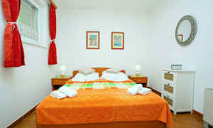 Makuuhuone, jossa on parisänky, oranssi päiväpeite, kaksi yöpöytää lampuilla ja seinäkoristeet. (Tekoälyn luoma teksti)