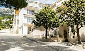 Valkoinen monikerroksinen rakennus parvekkeineen, jota ympäröi vihreys. (Tekoälyn luoma teksti)