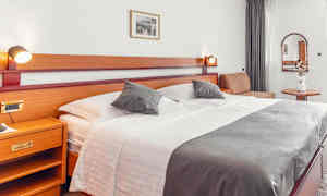 Hotellihuone, jossa suuri sänky, sivupöytä ja koristeita. (Tekoälyn luoma teksti)