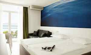 Kahden hengen huone, jossa suuri sininen seinämaalaus sängyn takana. Parveke merinäköalalla. (Tekoälyn luoma teksti)