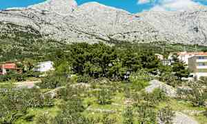 Kuva maisemasta, jossa rakennuksia, puita ja vehreyttä vuorten edessä. (Tekoälyn luoma teksti)