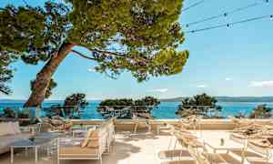 Ulkoilusterassi, jossa tuoleja ja pöytiä, näkymä merelle ja ympäröiville puille. (Tekoälyn luoma teksti)