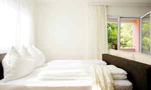 Valoisa huone, jossa sänky lähellä ikkunaa ja parveketta. (Tekoälyn luoma teksti)