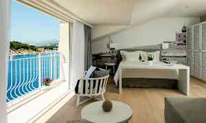 Hotellihuone, jossa on pedattu sänky, istuinalue ja parveke, josta näkyy merinäkymä. (Tekoälyn luoma teksti)