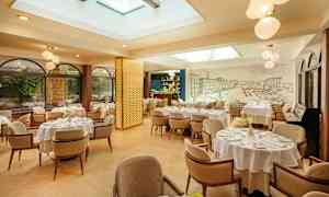 Valoisa ja tyylikäs ravintola, jossa pöydät ovat valkoisilla liinoilla ja mukavat tuolit. Ikkunat kasveineen ulkopuolella ja kattoikkunat tuovat luonnonvaloa. (Tekoälyn luoma teksti)