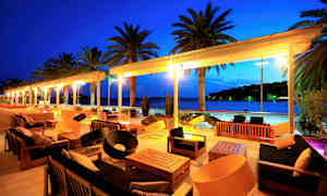 Ulkokalusteita terassilla, josta on näkymä merelle ja palmuihin illalla. (Tekoälyn luoma teksti)