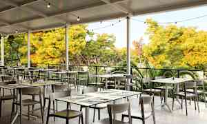 Ulkoravintola, jonka pöydät ja tuolit sijaitsevat katon alla, ympärillä vehreää luontoa. (Tekoälyn luoma teksti)