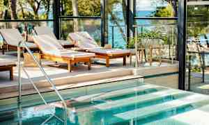 Aurinkotuoleja uima-altaan vieressä, näkymä merelle. (Tekoälyn luoma teksti)