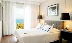 Valoisa hotellihuone, jossa on parivuode, moderni sisustus ja merinäköala suurista ikkunoista. (Tekoälyn luoma teksti)