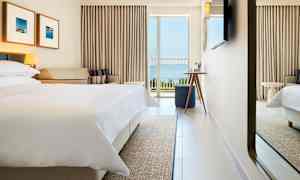 Hotellihuone, jossa pedattu sänky, sohva ja parveke merinäköalalla. (Tekoälyn luoma teksti)