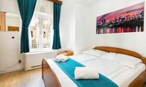 Makuuhuone, jossa on parivuode, turkoosit verhot ja seinällä kuva kaupungin siluetista. (Tekoälyn luoma teksti)