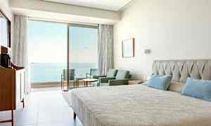 Hotellihuone, jossa sänky, istuinryhmä ja meri näkyy lasiovien läpi. (Tekoälyn luoma teksti)