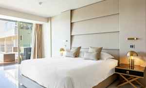 Moderni hotellihuone, jossa suuri sänky, tyylikäs sisustus ja näkymä terassille. (Tekoälyn luoma teksti)