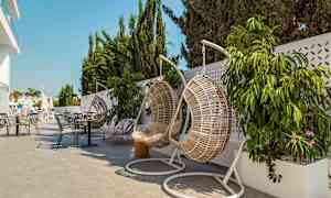 Riippuvat korituolit ja pöydät terassilla, jossa on kasveja ja aurinkovarjoja. (Tekoälyn luoma teksti)