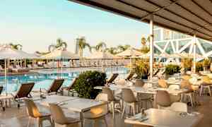 Uima-allasalue, jossa aurinkotuoleja, aurinkovarjoja ja ruokapöytiä veden äärellä. (Tekoälyn luoma teksti)