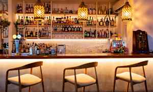 Baaritiski, jossa on tuoleja, hyllyt täynnä pulloja ja laseja. (Tekoälyn luoma teksti)