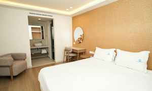 Hotellihuone, jossa on parivuode, kirjoituspöytä ja nojatuoli. Taustalla näkyy kylpyhuone. (Tekoälyn luoma teksti)