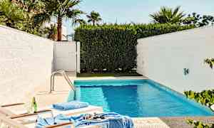 Pieni uima-allas, jota ympäröivät valkoiset seinät ja vihreä kasvillisuus, kaksi aurinkotuolia lähellä reunaa. (Tekoälyn luoma teksti)